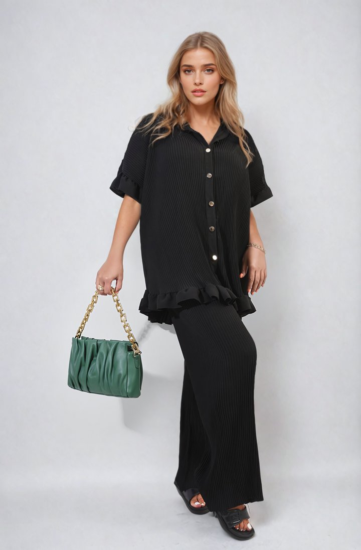 Woman in black outfit holds a green purse while wearing the Button Pleated Frill Ruffle Top and Wide Leg Trouser Co-ord Set, showcasing its stylish elegance.