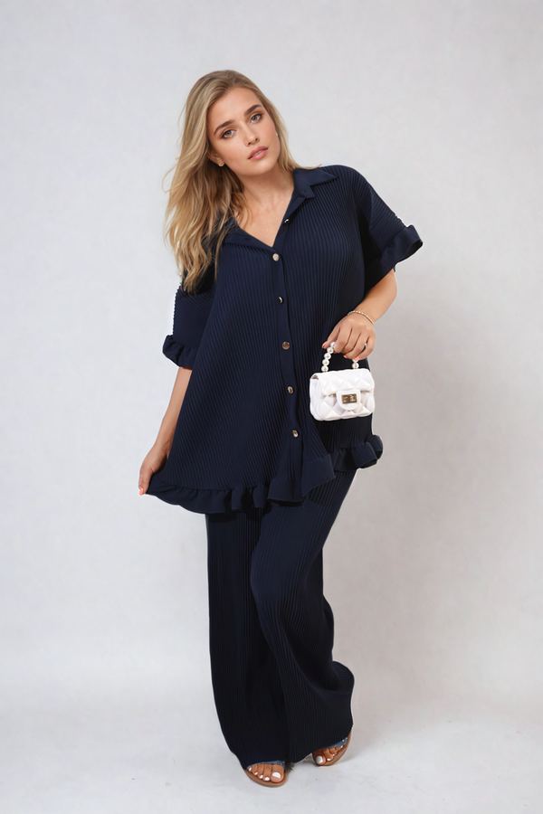 Woman wearing Emily Button Pleated Frill Ruffle Top and Wide Leg Trouser Co-ord Set, holding a white purse, showcasing chic holiday-ready style.