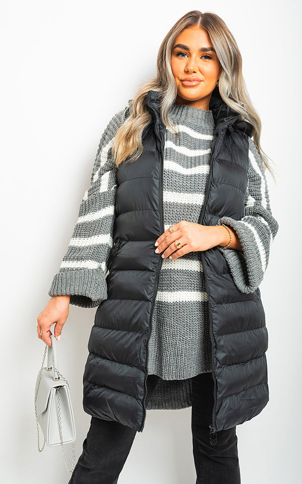 Woman wearing a Hooded Longline Quilted Gilet with a black puffy vest and sweater, accessorized with a white purse, highlighting stylish winter fashion essentials.