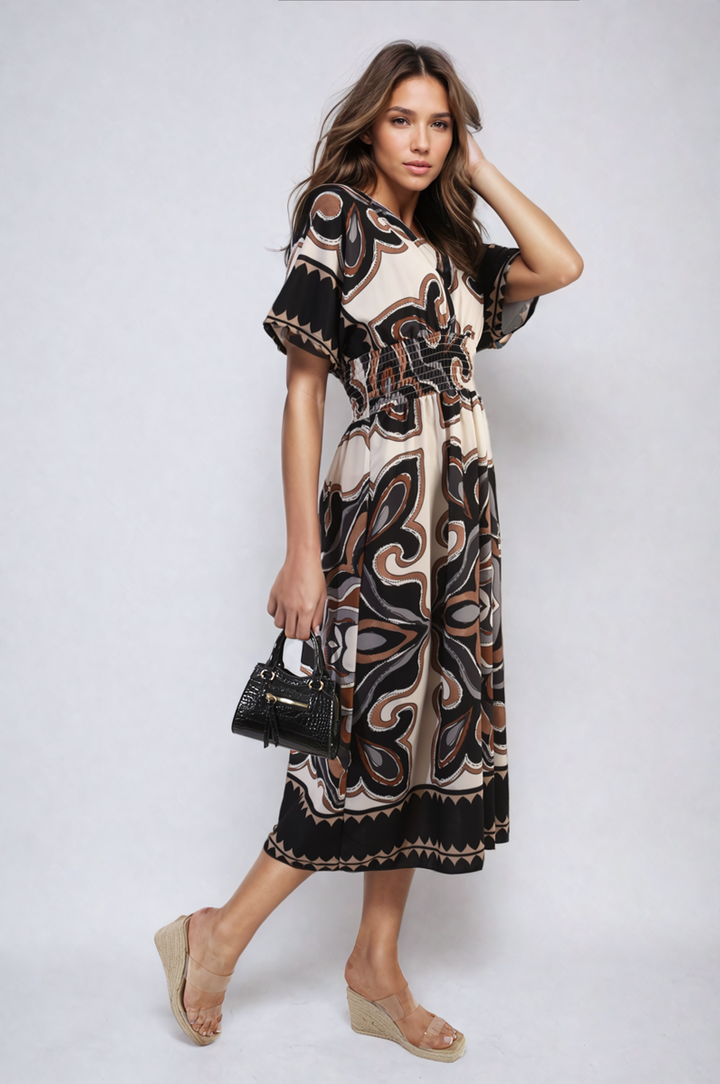 Woman modeling the Ruched Printed V-Neck Short Sleeve Midi Dress, holding a purse, showcasing its ruched design and chic pattern, ideal for casual occasions.