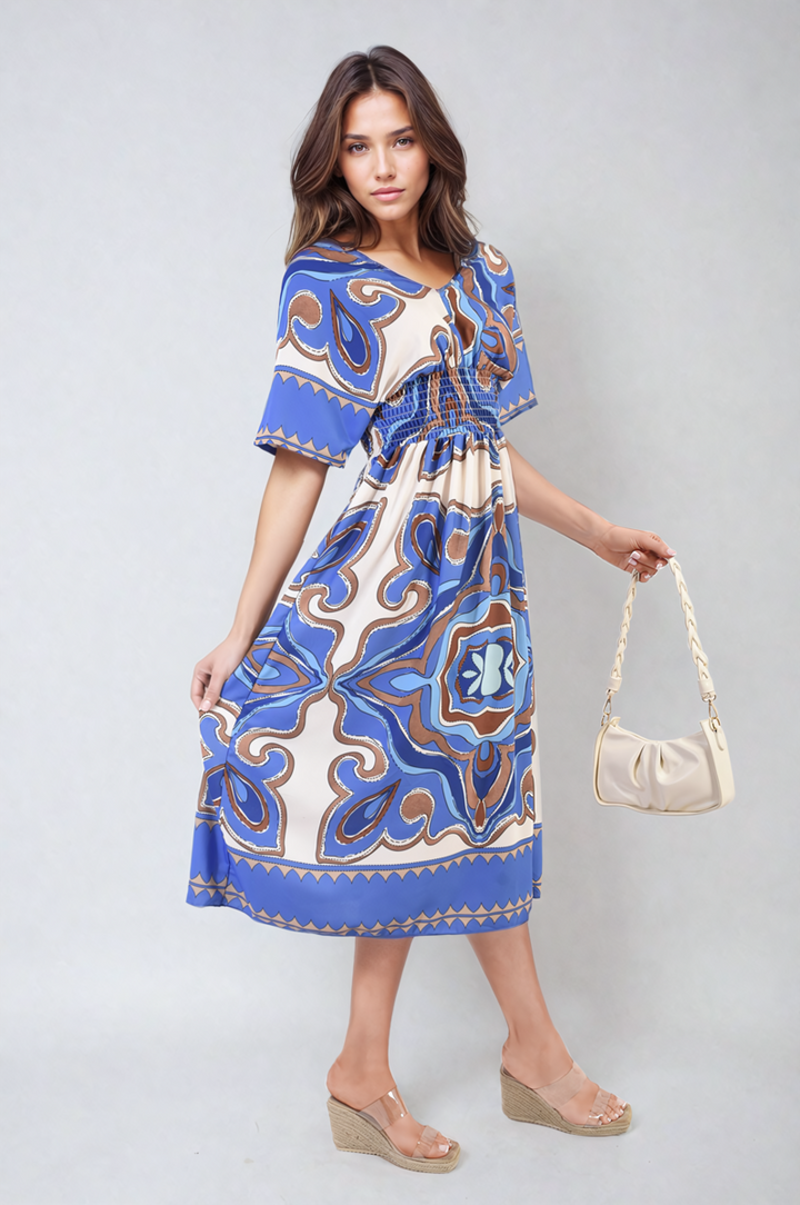 Woman wearing the Ruched Printed V-Neck Short Sleeve Midi Dress, paired with a white braided-strap purse and sandals, embodying casual elegance from Holiday Clothes UK.