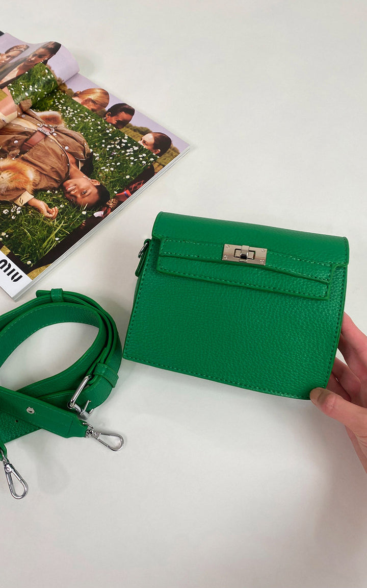 A hand holds the Faux Leather Crossbody Bag with Adjustable Strap, featuring a silver clasp, next to a magazine.