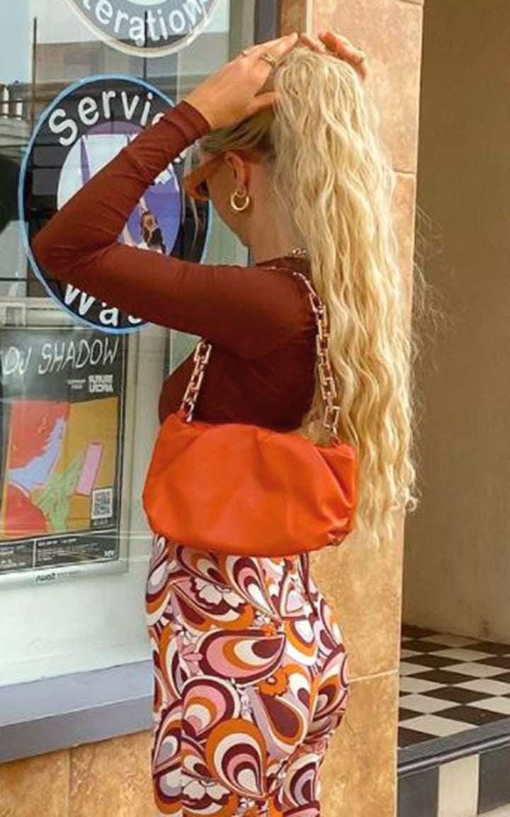 Woman with long blonde hair holds the Eve Faux Leather Shoulder Bag with Chain Detail, showcasing its chic design and spaciousness, ideal for everyday use.