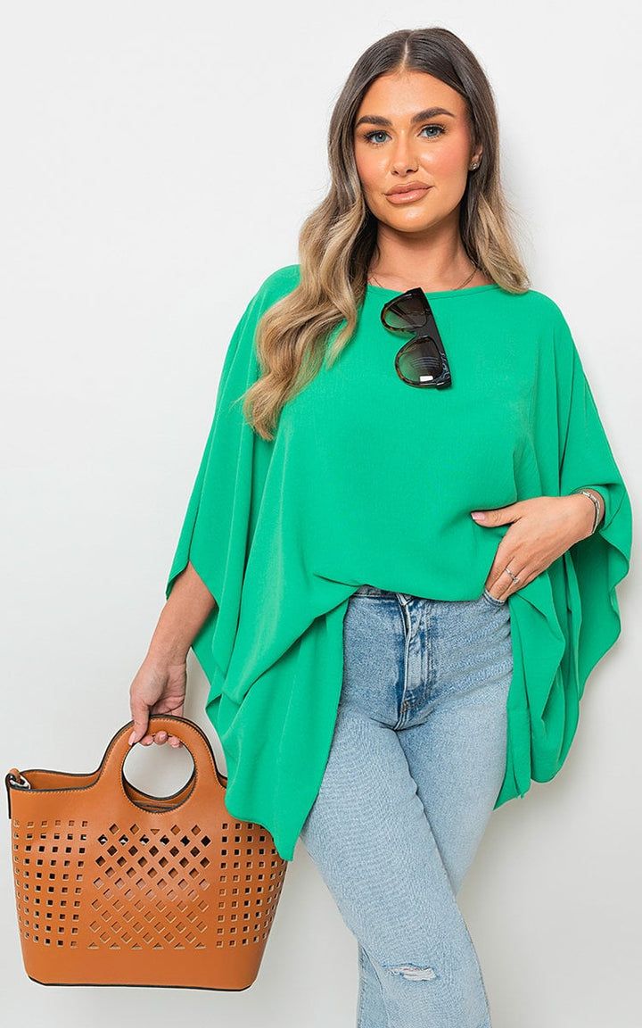 Woman in green top holding a brown Oversized Batwing Sleeve Casual Top, showcasing its relaxed fit and stylish batwing sleeves.