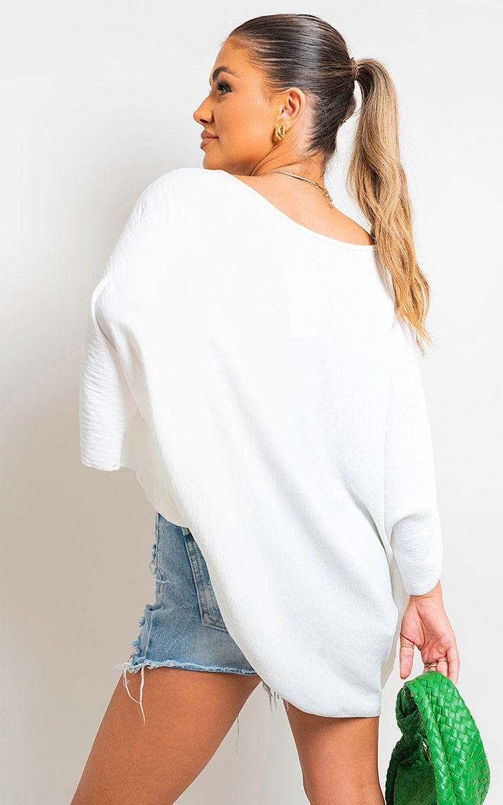 Woman in white top holding green bag, showcasing the Fatima Oversized Batwing Sleeve Casual Tops, emphasizing its relaxed and stylish design.