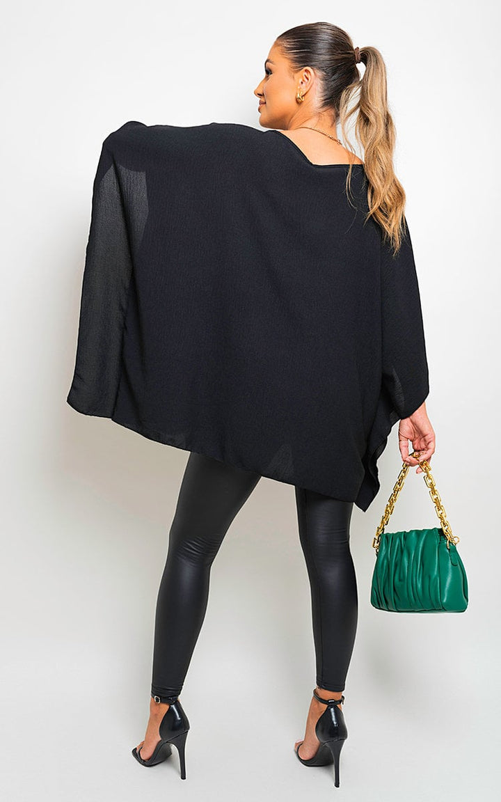 Woman in black top with batwing sleeves holding a green purse, showcasing the Fatima Oversized Batwing Sleeve Casual Tops from Holiday Clothes UK.