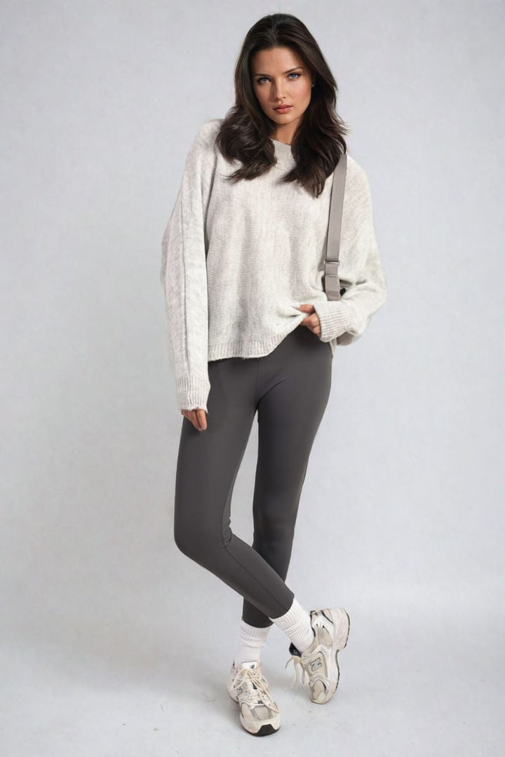 Woman wearing Florencia Crew Neck Back Patterned Knitted Jumper, posing indoors, showcasing the jumper's unique back design, paired with grey pants and white sneakers.