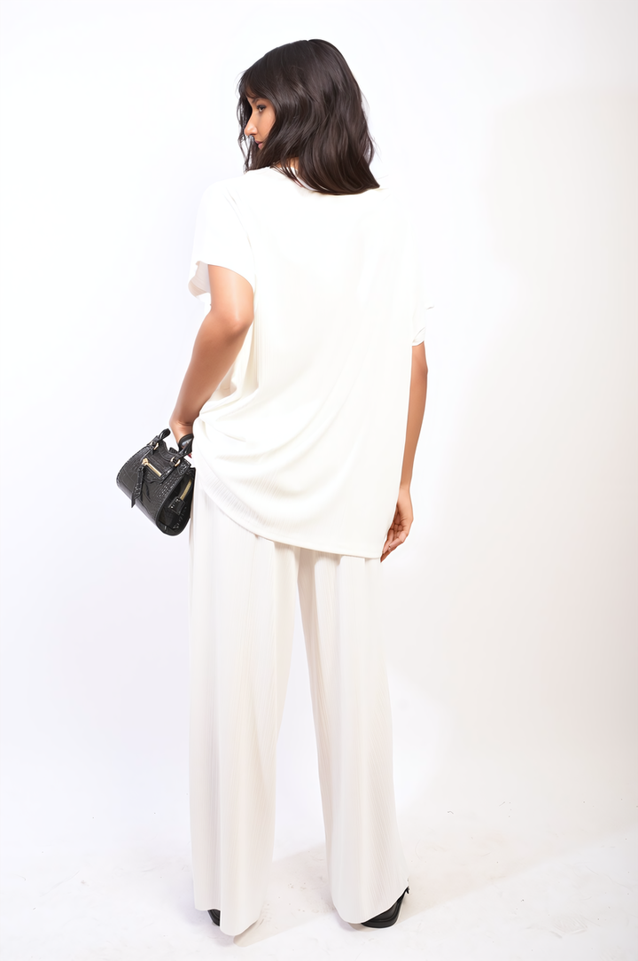 Woman in a white oversized top and wide leg trouser co-ord set, accessorized with a black purse, embodying relaxed elegance and modern style.