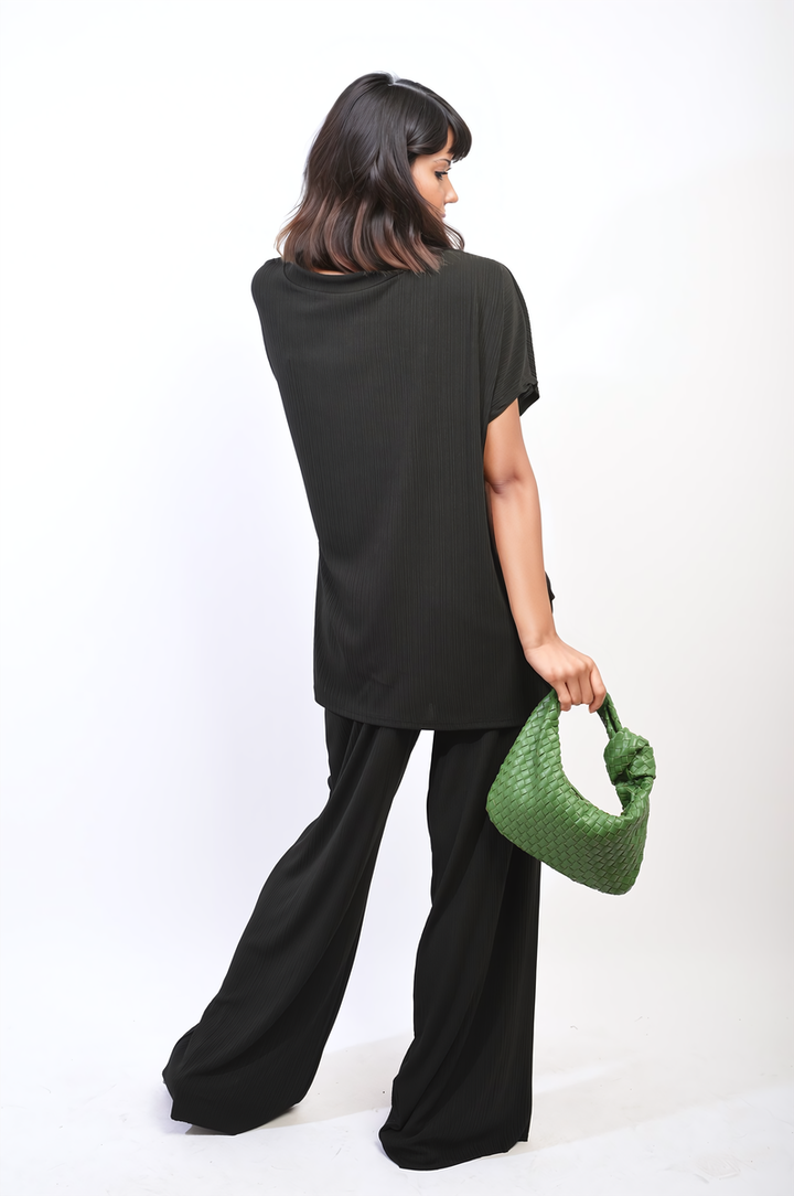 Woman in black outfit holding a green purse, showcasing the Oversized Top and Wide Leg Trouser Co-ord Set from Holiday Clothes UK.