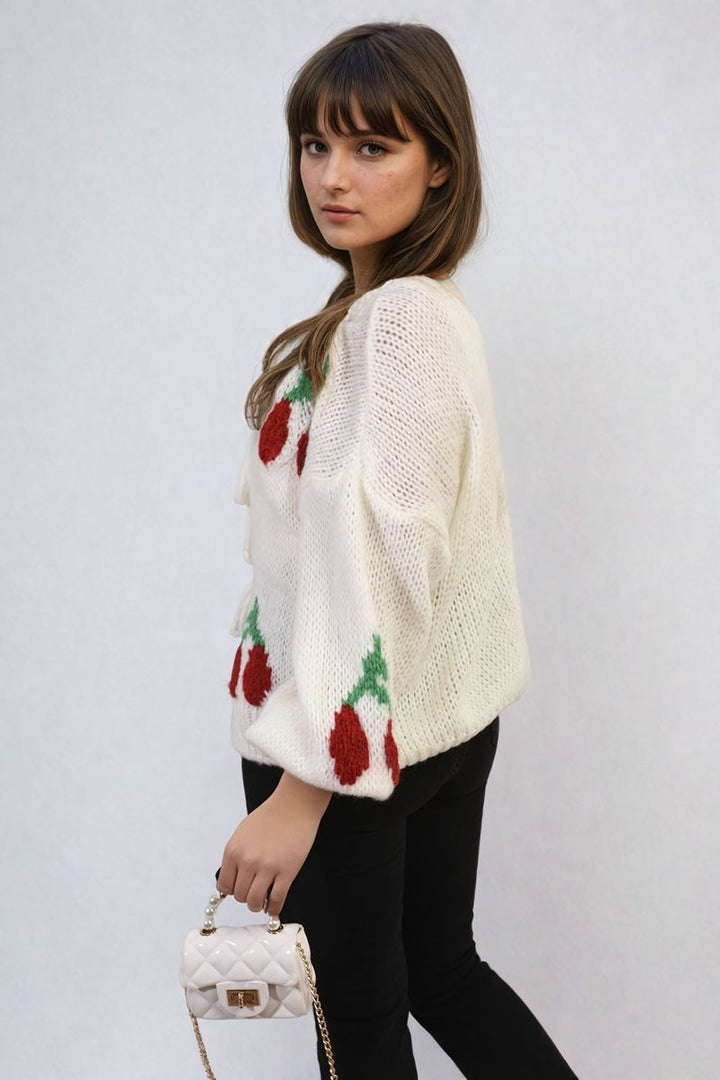 Woman in a tie front cherry print knitted cardigan, featuring playful patterns and a cozy knit, holding a white purse.