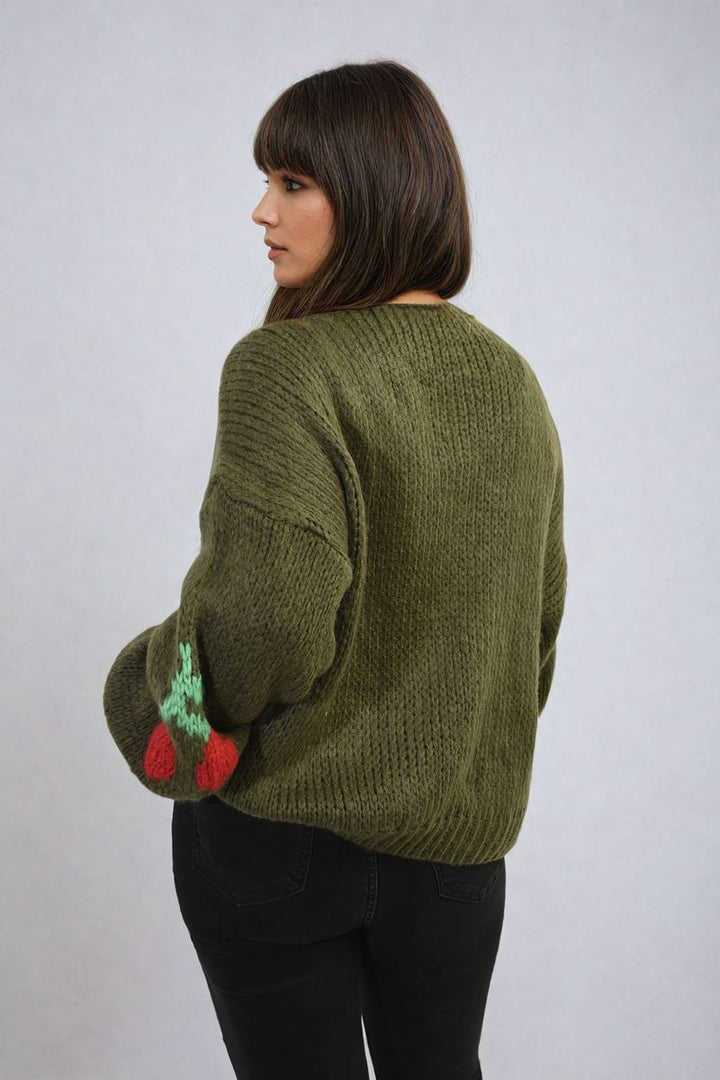 Woman in a green sweater showcasing the Giselle Tie Front Cherry Print Knitted Cardigan with a charming cherry design and tie front detail.