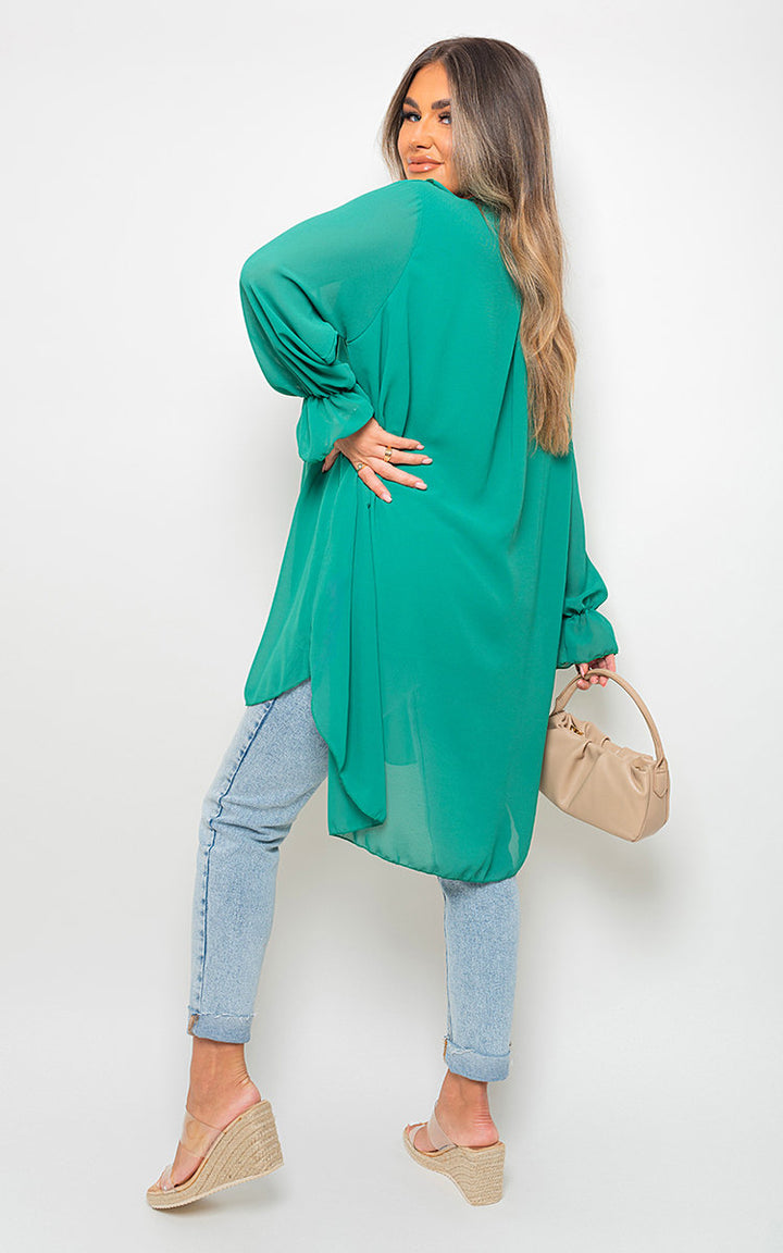 Woman wearing Oversized Ruffle Long Sleeve Top, showcasing its draped fit and ruffle sleeve detail, holding a purse. Perfect blend of comfort and style.