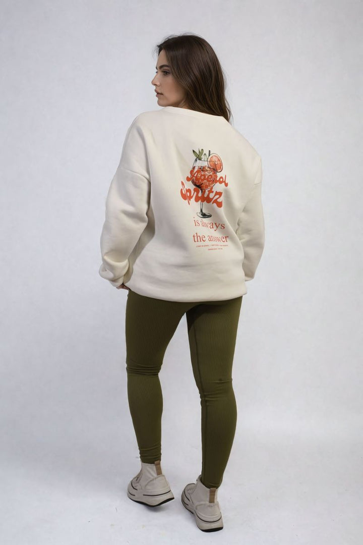 Woman wearing the Helen Aperol Spritz Cocktail Graphic Knitted Jumper, featuring a playful cocktail design, paired with green pants and white shoes.