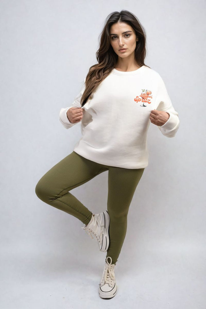 Woman wearing the Helen Aperol Spritz Cocktail Graphic Knitted Jumper, featuring a fun cocktail design, paired with casual trousers and white sneakers.