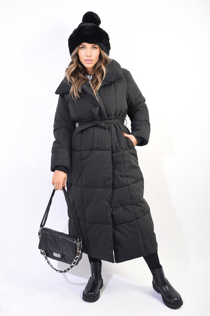 Woman wearing the Irene Longline Puffer Jacket with Belt Detail, featuring a cinched waist and cozy hood, perfect for stylish winter warmth.