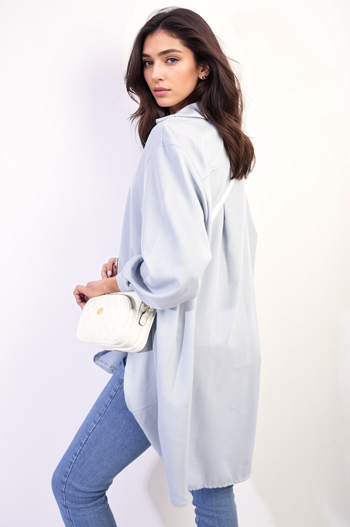 Woman wearing Button Up Oversized Long Back Shirt Dress, holding a white purse, styled with blue jeans, embodying effortless chic and versatile fashion.