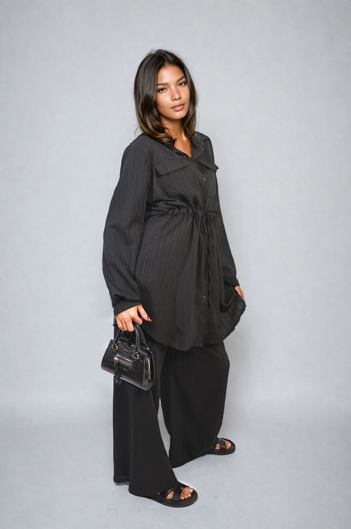 Woman wearing the Oversized Long Sleeve Belted Button Down Top and Trouser Co-ord Set, holding a black purse, showcasing a stylish and coordinated look.