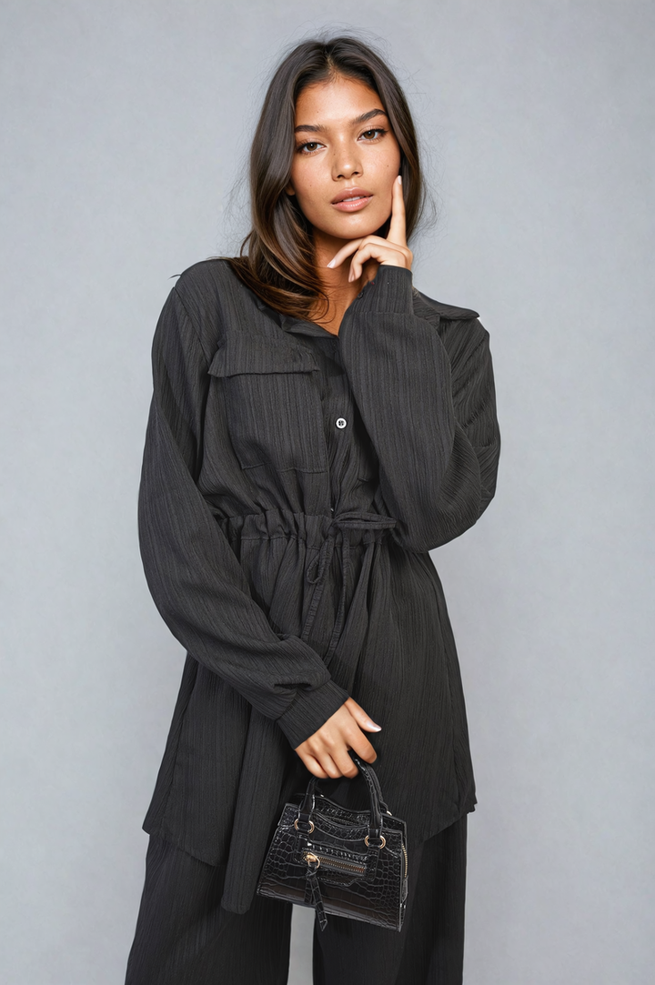 Woman in a black dress holds a close-up of the Oversized Long Sleeve Belted Button Down Top and Trouser Co-ord Set, showcasing its chic, versatile design.