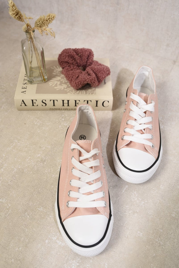 Pink sneakers with white laces, known as Jenna Platform Low Top Lace Up Trainers, displayed beside a book on a white surface.