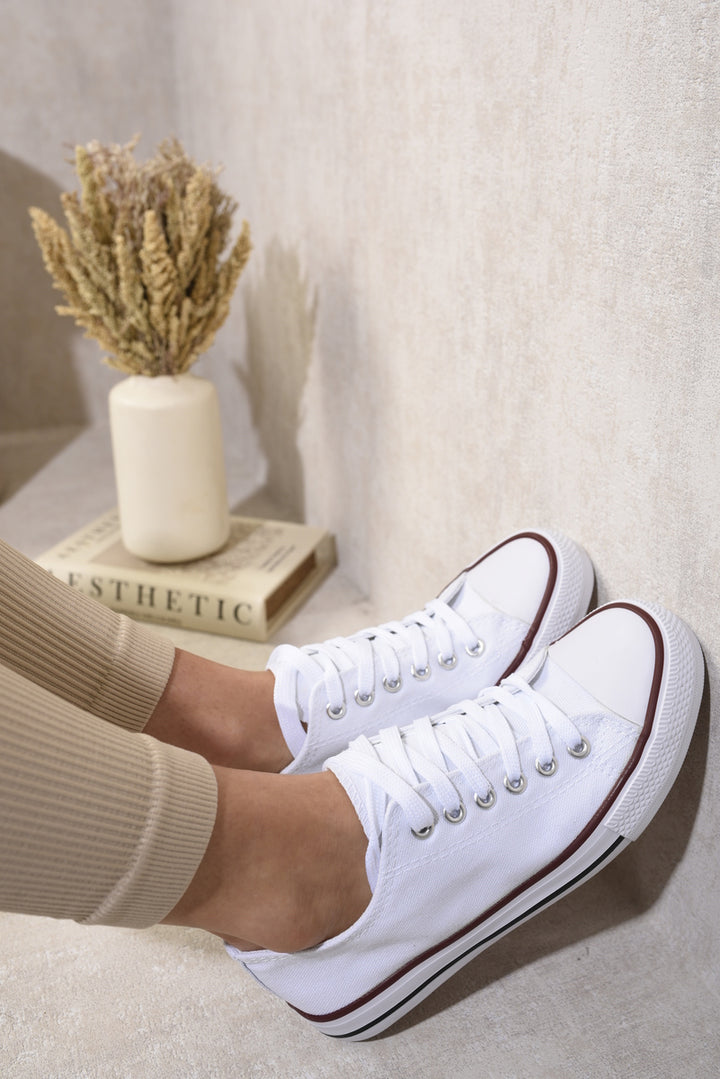 White Platform Low Top Lace Up Trainers with a chic design and comfortable fit, perfect for casual wear. Featured alongside a vase and book for stylish presentation.