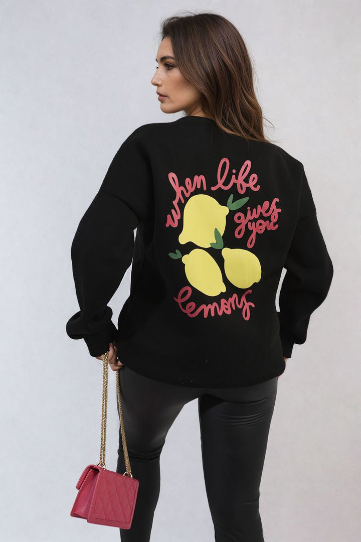 Woman wearing the Joyce Lemon Graphic Long Sleeve Knitted Jumper, featuring a playful lemon design, paired with black pants, embodying cozy and stylish fashion.