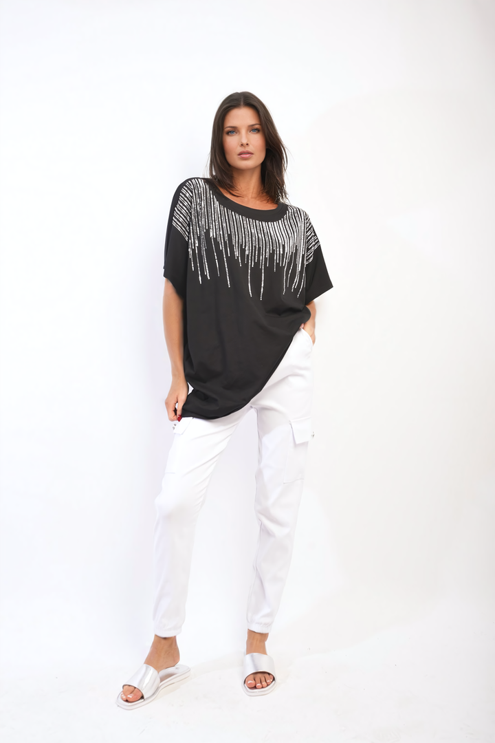 Woman wearing the Juliana Embellished Neckline Short Sleeve Top, posing with white pants, showcasing its chic style for casual elegance.