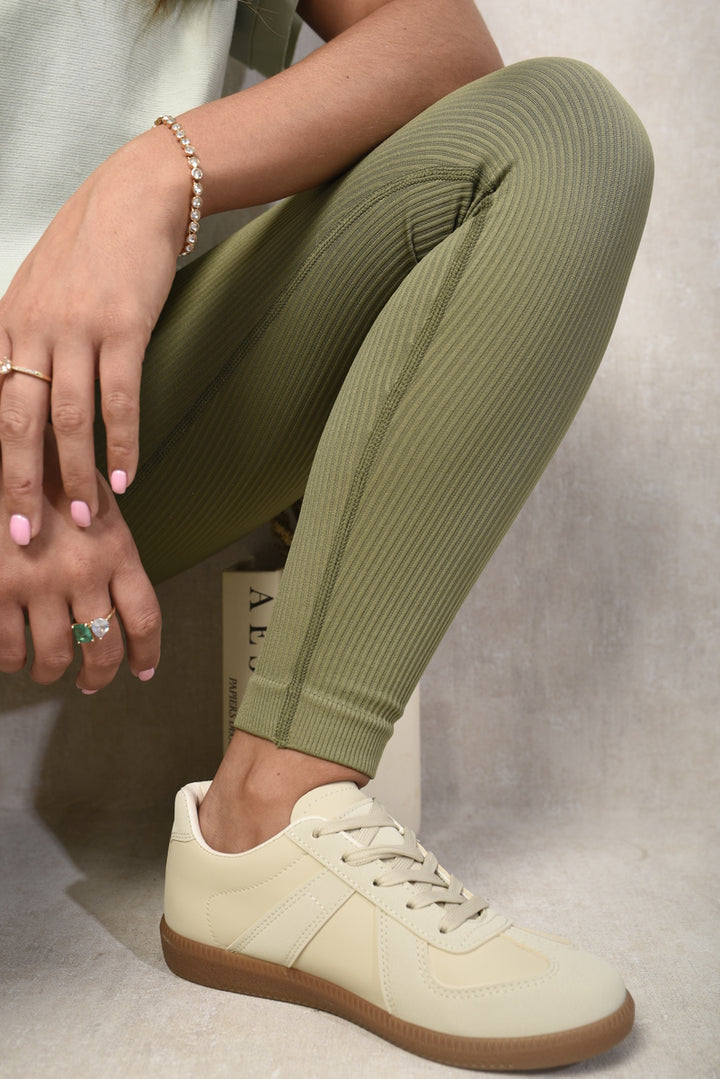 Person wearing Julissa Low Top Lace-Up Trainers with white sneakers and green leggings. The close-up highlights the shoe's modern design and comfort features.