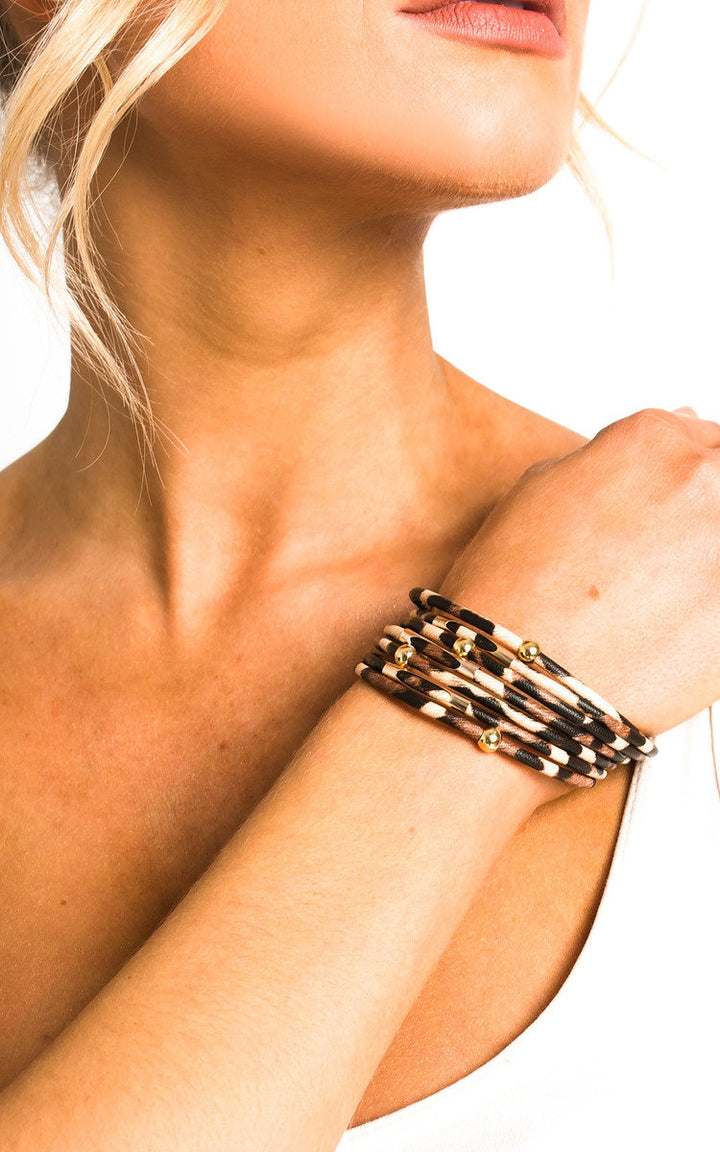 Woman wearing the Leopard Print Bracelet, featuring a leopard design with multi straps, gold beads, and a clasp fastening, perfect for stylish holiday looks.