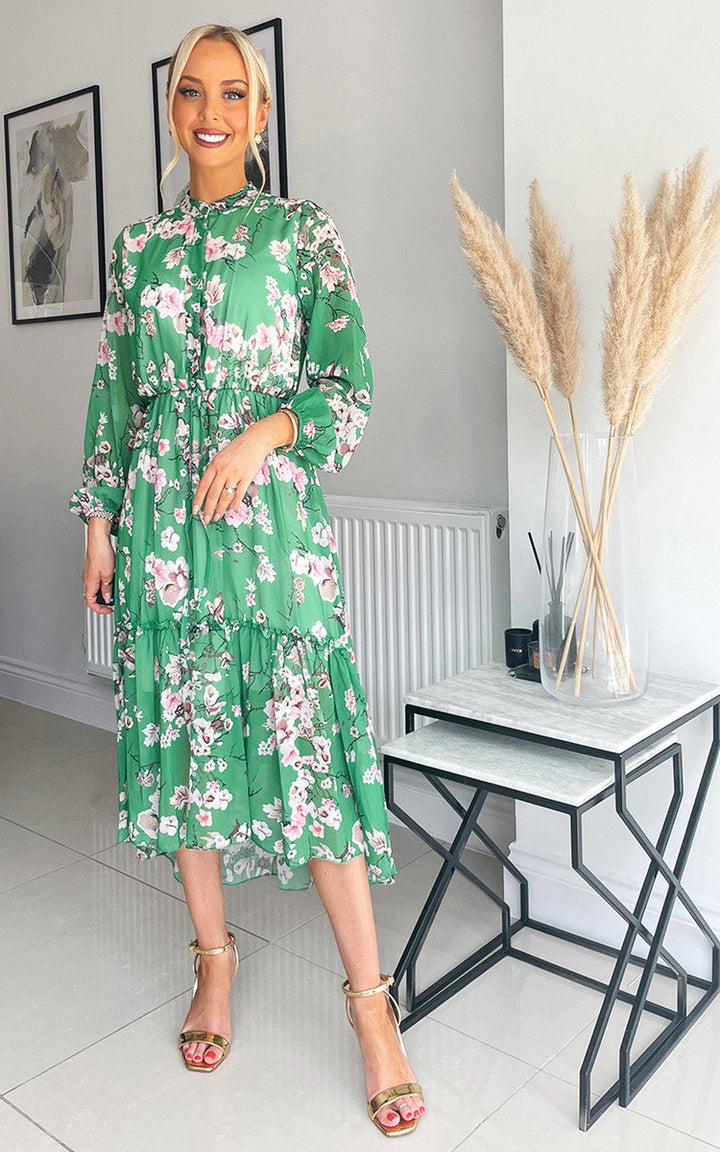 Woman in a green Tiered Midi Dress, part of Holiday Clothes UK's stylish holiday collection, standing near a marble table, smiling confidently.