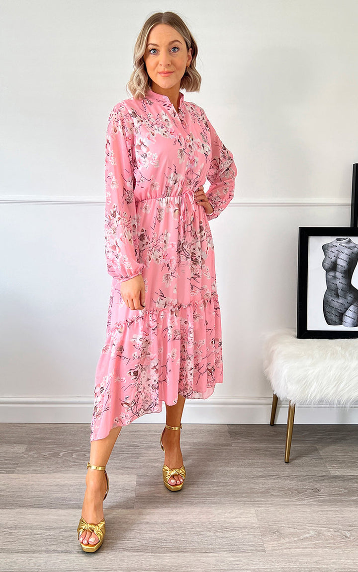 Woman wearing the Laila Tiered Midi Dress with floral print, paired with gold sandals, standing indoors. Perfect for a stylish, carefree summer look.