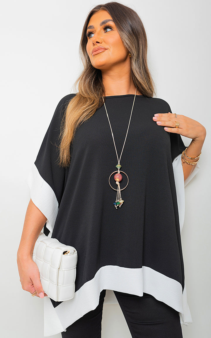 Woman wearing an Oversized Contrast Hem Flare Sleeve Top with flared sleeves, holding a white purse and wearing a silver necklace.