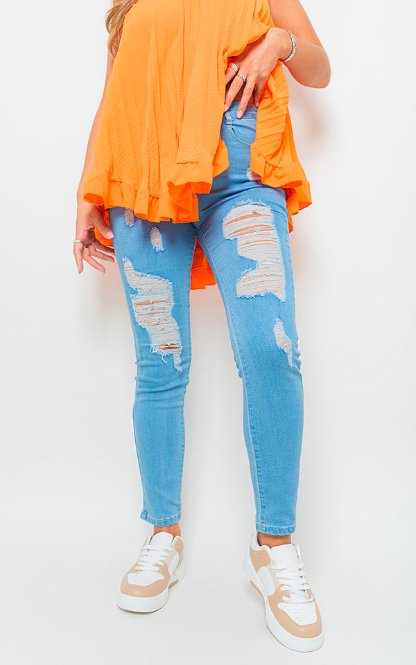 Person wearing Lauren Distressed High Waisted Jeans with ripped detailing, paired with white sneakers and an orange top, embodying a chic, edgy style.