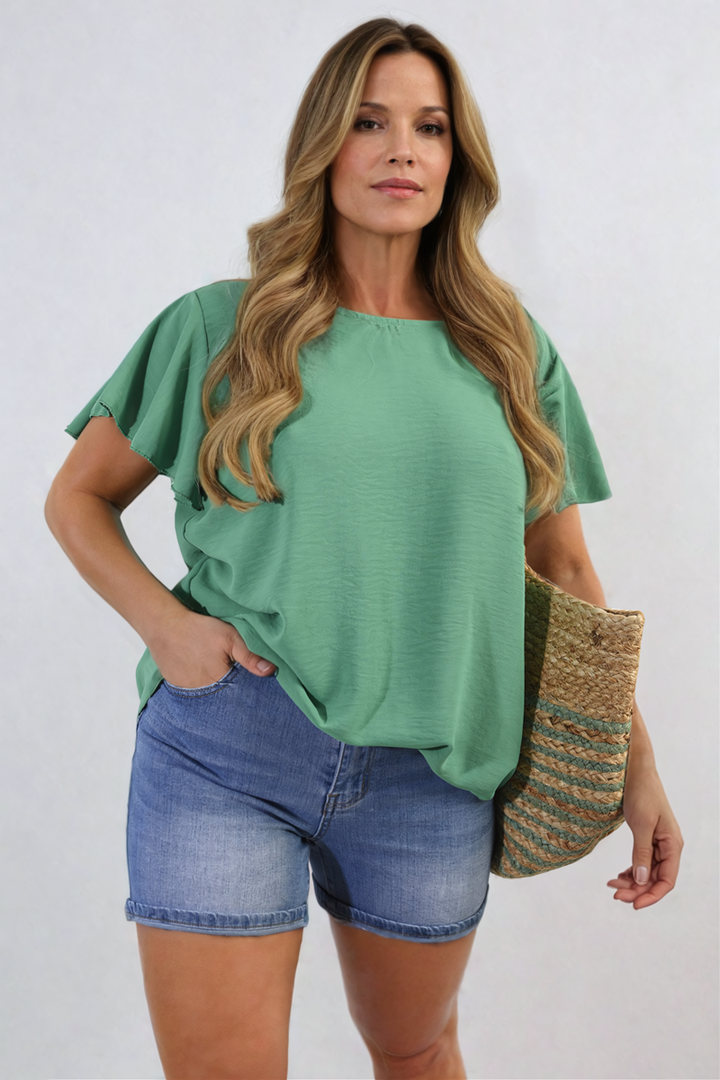 Woman wearing Leilani Ruffle Short Sleeve Top with ruffled sleeves, paired with blue jean shorts, showcasing a casual yet stylish look from Holiday Clothes UK.