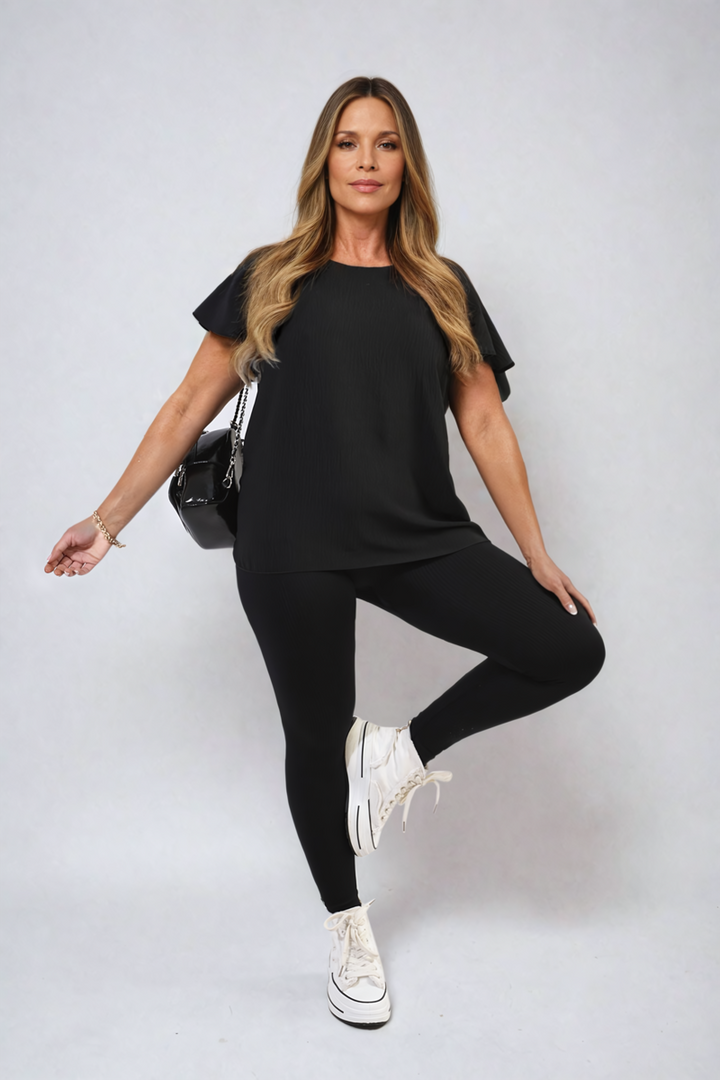 Woman wearing a black dress holds the Leilani Ruffle Short Sleeve Top, showcasing its elegant ruffled sleeves for stylish holiday outfits at Holiday Clothes UK.