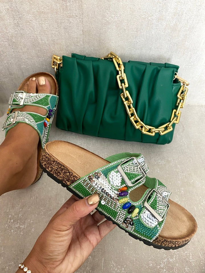 Hand holding Rhinestone Double Buckle Adjustable Slip-On Slides Sandals, showcasing their chic design and sparkling rhinestone buckles next to a green purse with a gold chain.