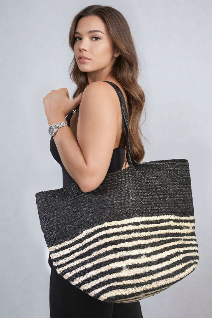 Woman in a black dress holding the Louisa Striped Beach Braided Tote Bag, showcasing its chic striped design and braided handles.