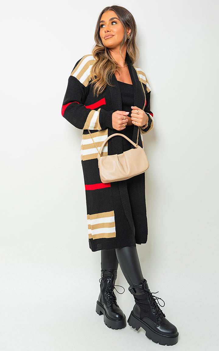 Woman wearing Oversized Long Striped Knitted Cardigan with black boots and holding a tan purse, showcasing cozy and chic fashion from Holiday Clothes UK.