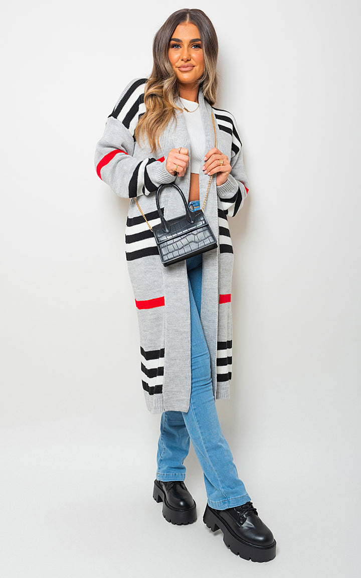 Woman wearing an Oversized Long Striped Knitted Cardigan with blue jeans, holding a black purse. The cardigan is styled for cozy, chic fashion.