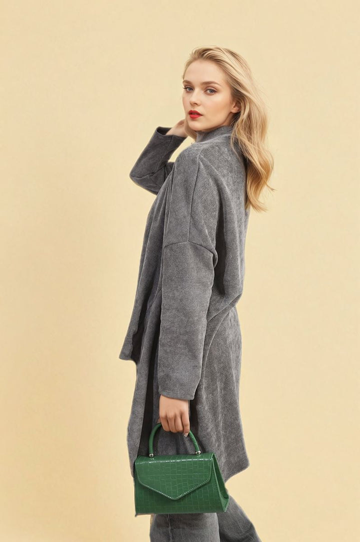 Woman in a grey knitted cardigan, the Lydia Open Front Long Back design, holding a green purse, embodying casual elegance for versatile styling.