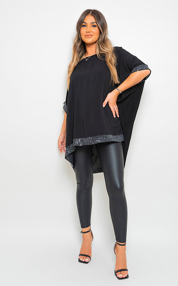 Woman showcasing the Oversized Sequin Trim Top, featuring a relaxed fit and chic sequin details, paired with black leggings and sandals.