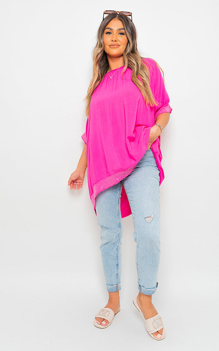 Woman in pink Oversized Sequin Trim Top, showcasing its relaxed fit and sequin accents, paired with jeans and sandals, highlighting casual elegance.