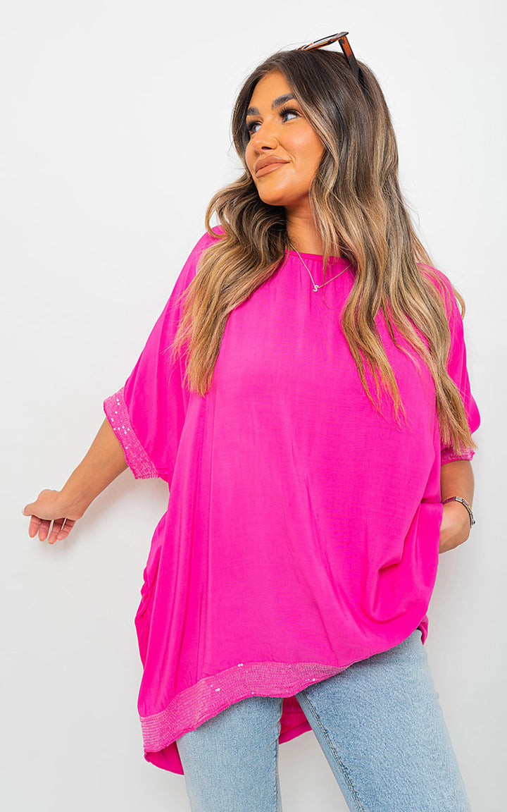 Woman in pink Lydia Oversized Sequin Trim Top, showcasing its relaxed fit and sequin details, perfect for casual or dressy occasions.