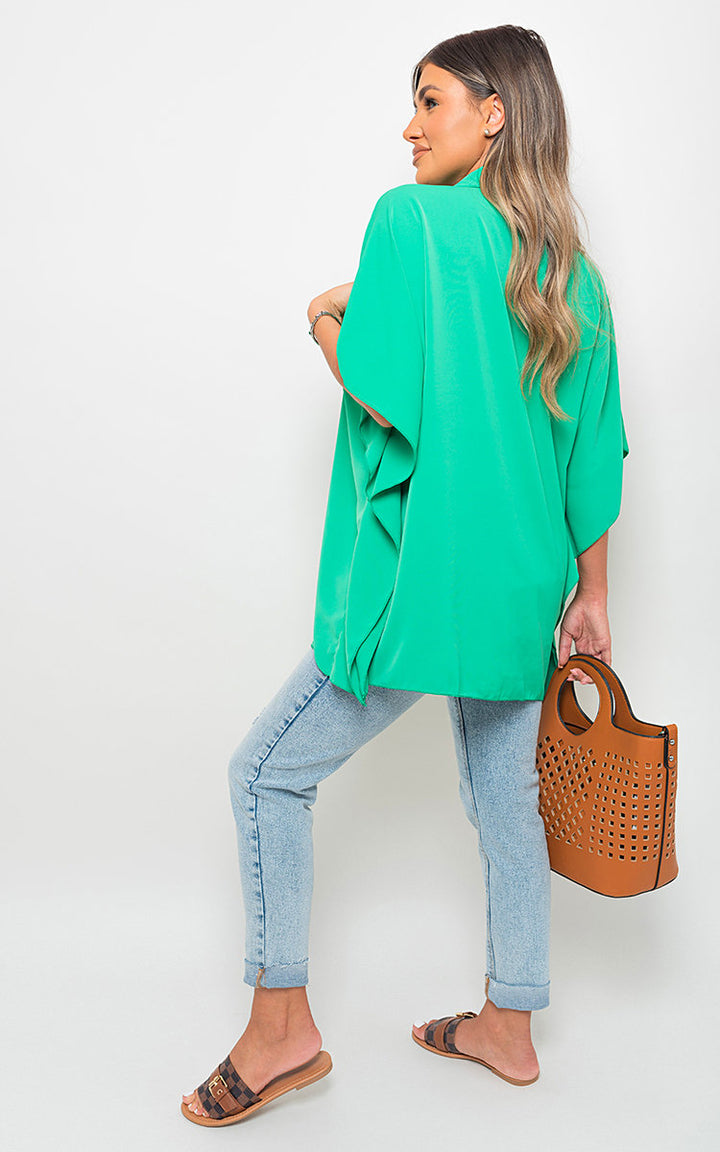 Woman in a green top and blue jeans holding a brown purse, showcasing the Button Down V Neck Casual Loose Tops from Holiday Clothes UK.