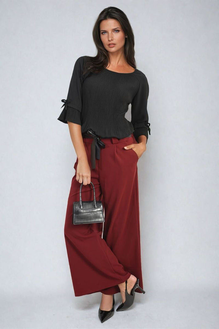 Woman showcases Belted High Waist Wide Leg Trouser, featuring a stylish high waist and wide leg design, complemented by a black shirt and purse.