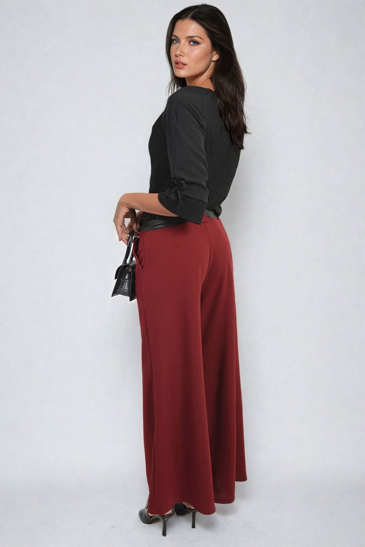 Woman wearing Belted High Waist Wide Leg Trouser, holding a purse. The trousers feature a flattering high waist and trendy wide leg design, ideal for various occasions.