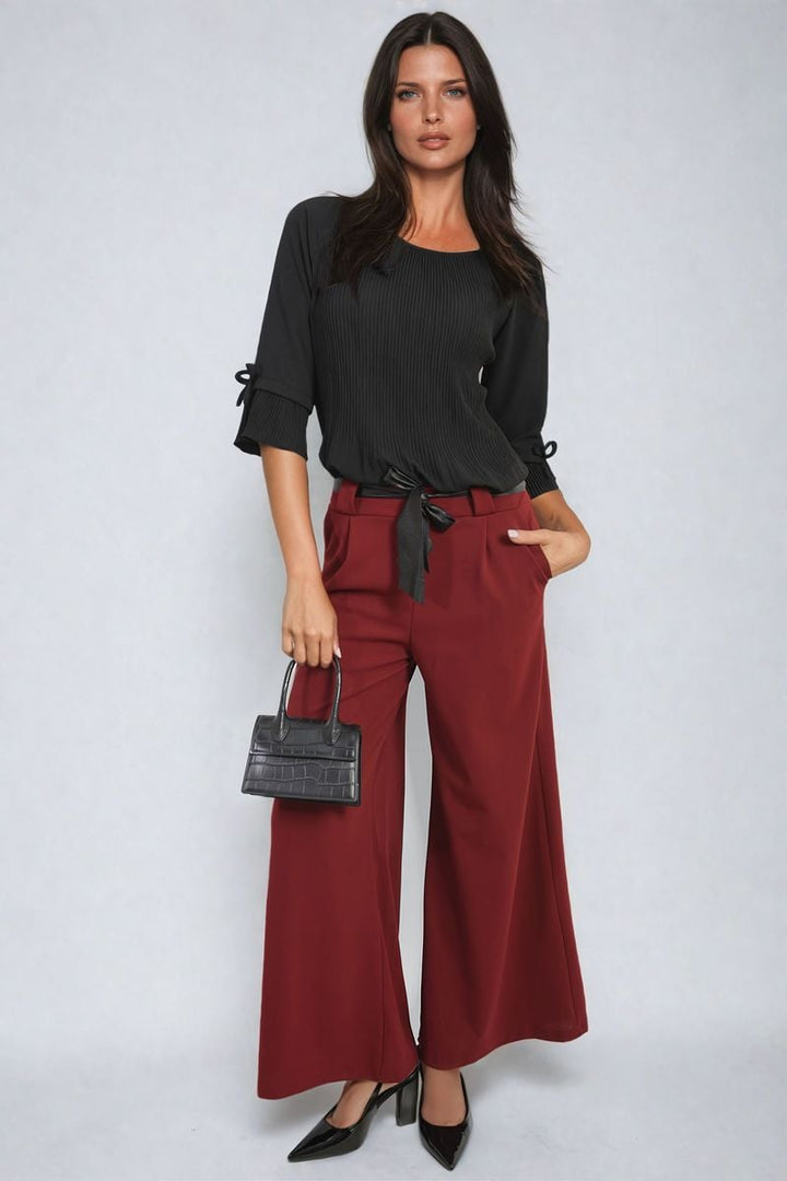 Woman modeling the Belted High Waist Wide Leg Trouser with a stylish silhouette, paired with high heels and a black purse.