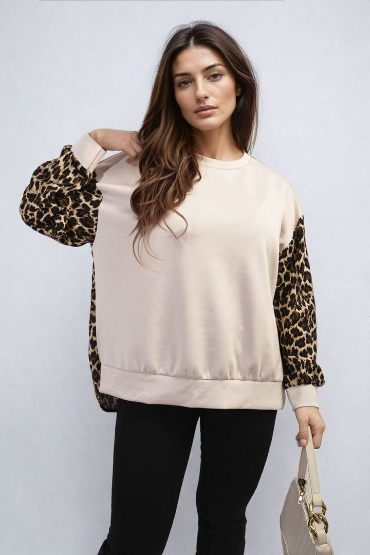 Woman in a leopard print long sleeve knitted jumper holding her shoulder, showcasing the Marissa jumper's stylish design and cozy fit.