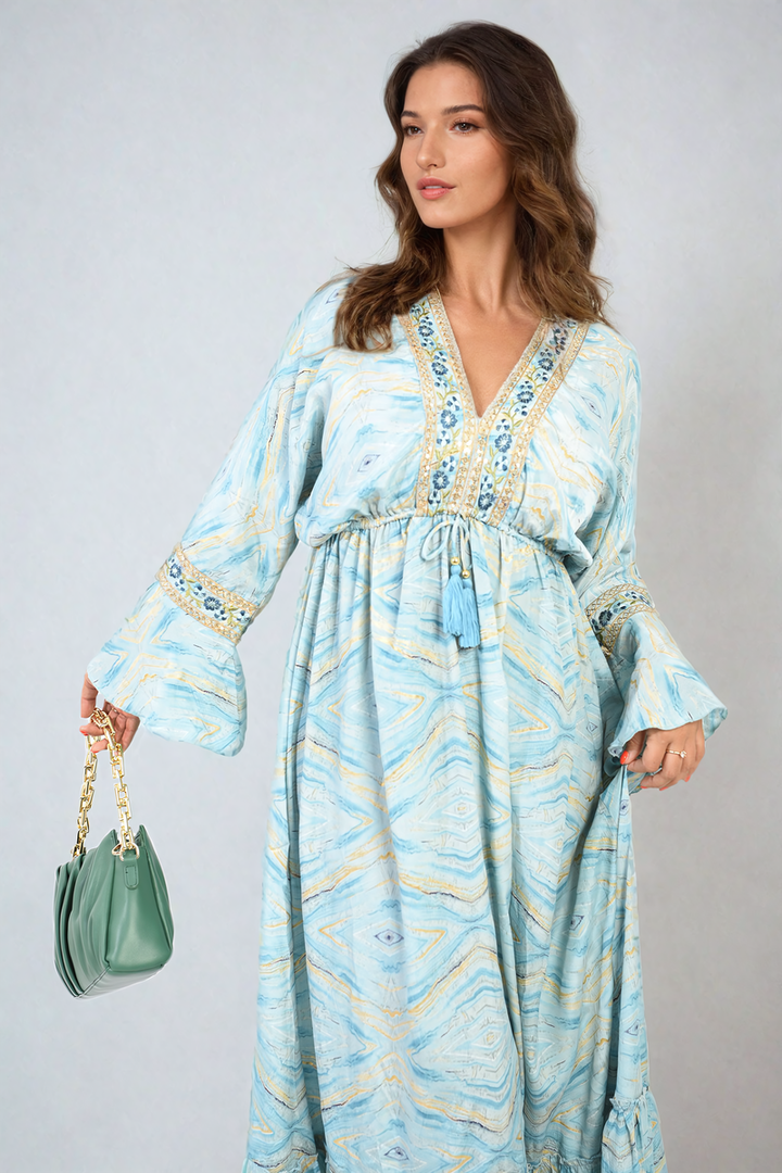 Woman wearing a Printed Long V-Neck Ruffled Hem Maxi Dress with Front Tassel Detail, holding a green purse with gold chains.