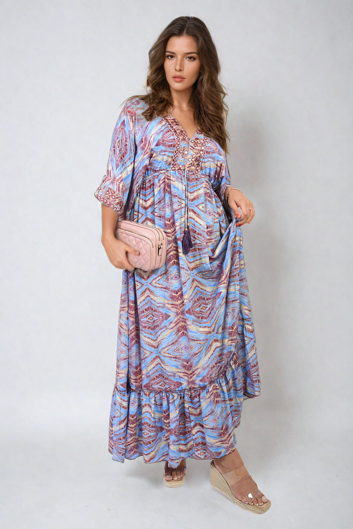 Woman in a printed long V-neck ruffled hem maxi dress, holding a pink purse, showcasing front tassel detail, epitomizing boho-chic fashion.