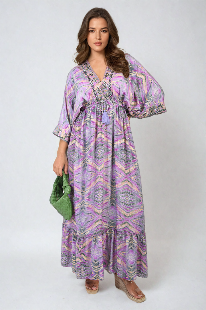 Woman wearing a Printed Long V-Neck Ruffled Hem Maxi Dress with Front Tassel Detail, showcasing a boho-chic style, standing gracefully indoors.